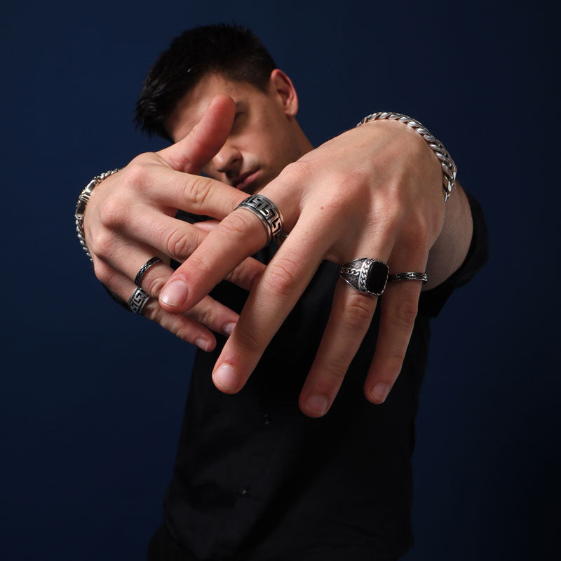 Man wearing multiple stylish 925 sterling silver rings and bracelets, showcasing bold and intricate men's jewelry designs against a dark blue background.