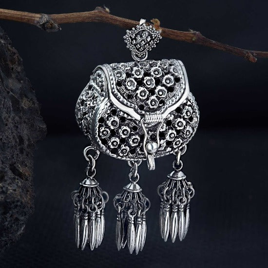 A sterling silver pendant in the shape of a handbag with an oxidized finish, featuring intricate details and hanging from a chain.