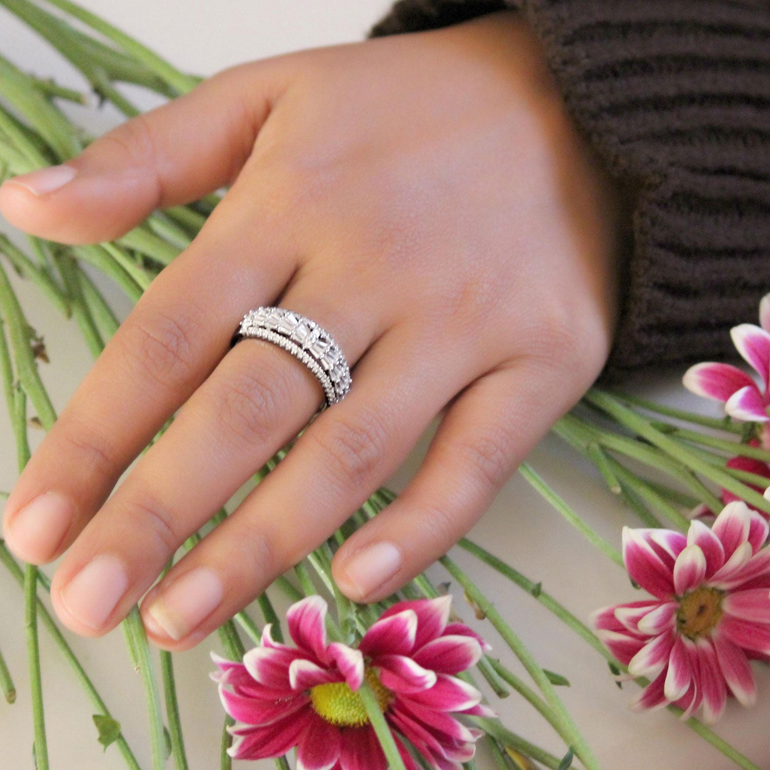 Hand wearing a silver ring with flowers in the background